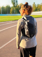 Person with a black backpack on a running track with trees in the background