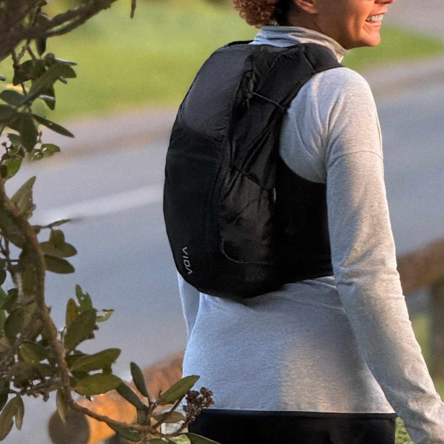 Person with a backpack walking outdoors near a road and trees